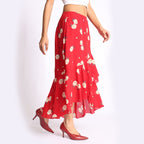 Woman wearing a red floral ruffle skirt with a black sleeveless crop top, styled with black heels and a textured handbag