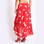 Woman wearing a red floral ruffle skirt with a black sleeveless crop top, styled with black heels and a textured handbag