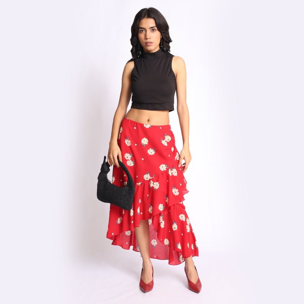 Woman wearing a red floral ruffle skirt with a black sleeveless crop top, styled with black heels and a textured handbag