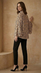 Woman wearing a leopard print blouse and black pants against a beige wall.