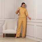 Woman in a yellow patterned outfit standing against a white paneled wall.