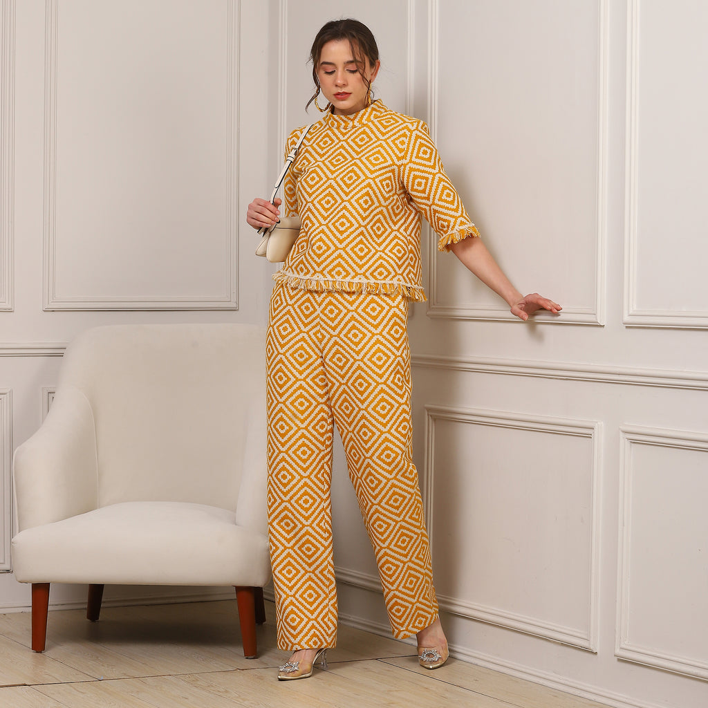 Woman in a yellow patterned outfit standing against a white paneled wall.