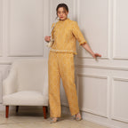 Woman in a yellow patterned outfit standing against a white paneled wall.