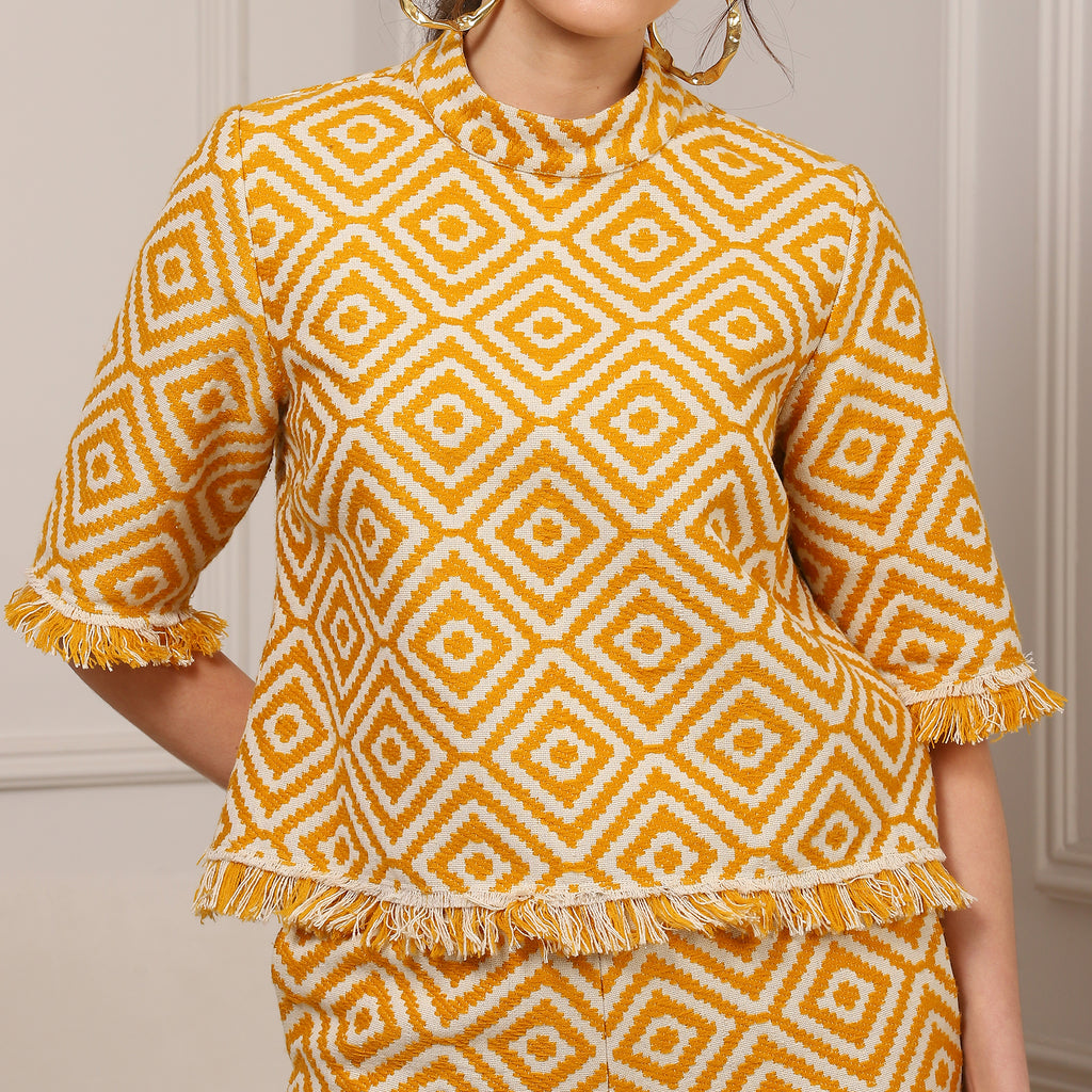 Person wearing a yellow and white patterned top with fringes on a neutral background