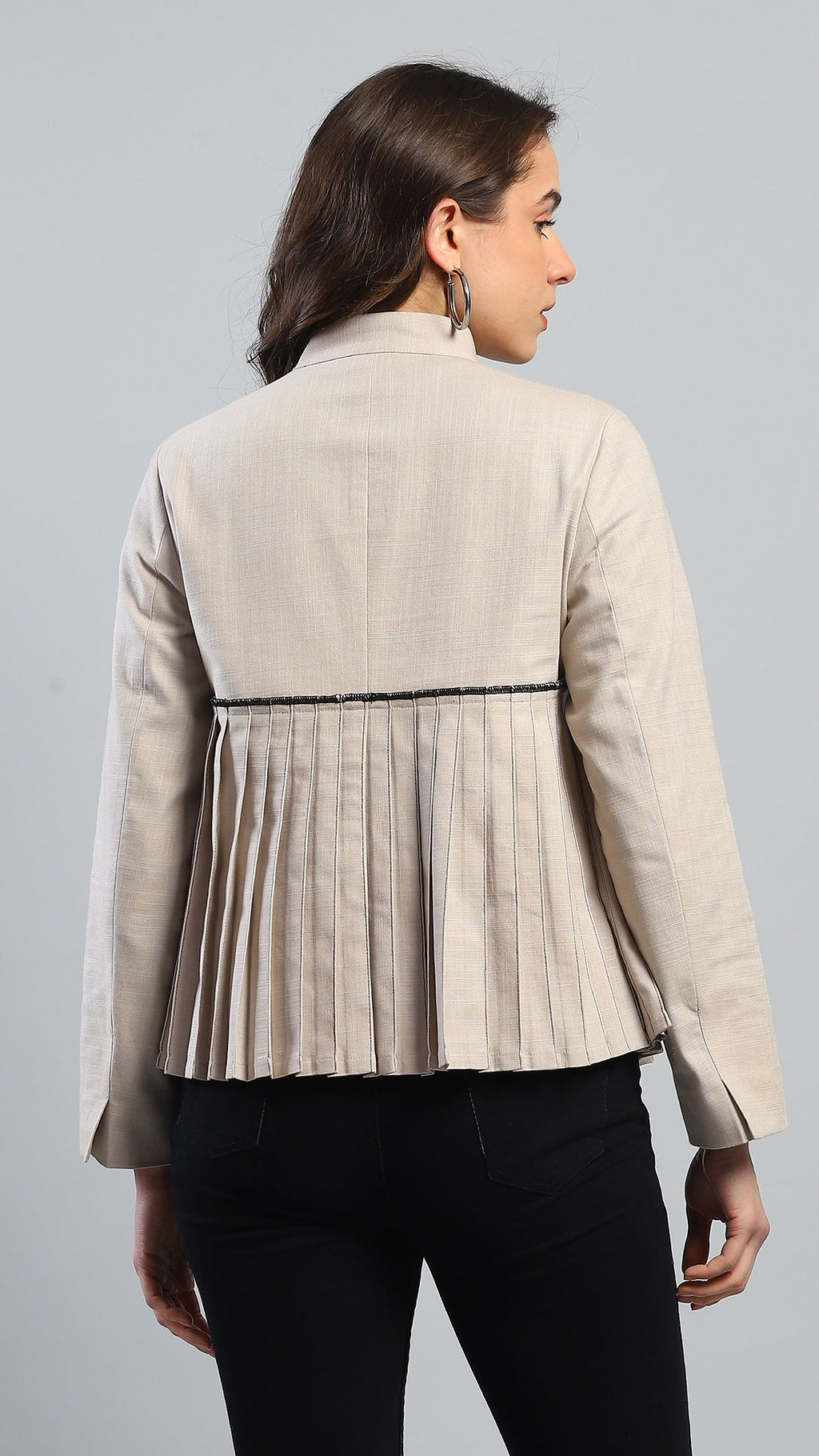 Woman wearing a beige blazer with a pleated design on a gray background