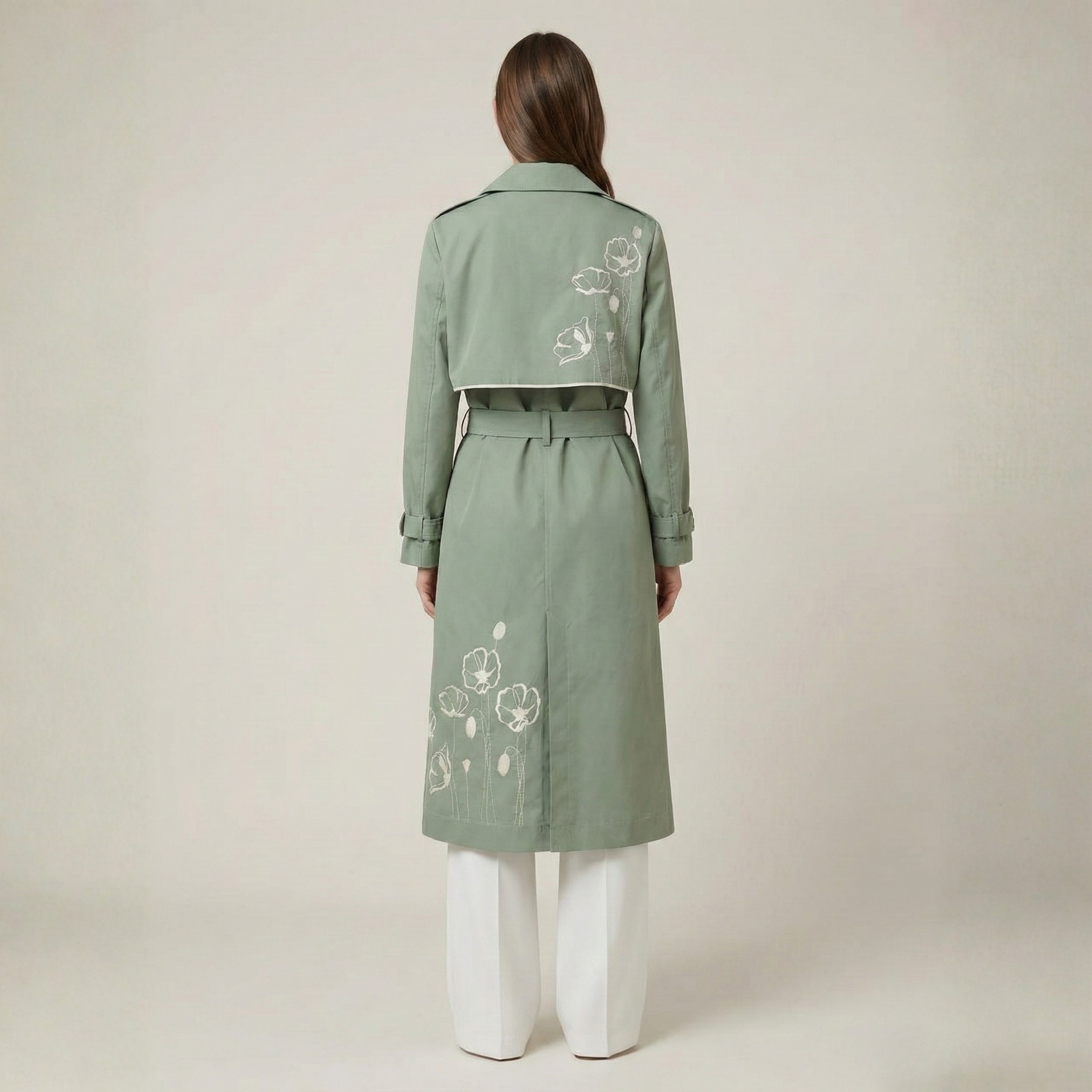 Person wearing a green trench coat with floral embroidery on a beige background