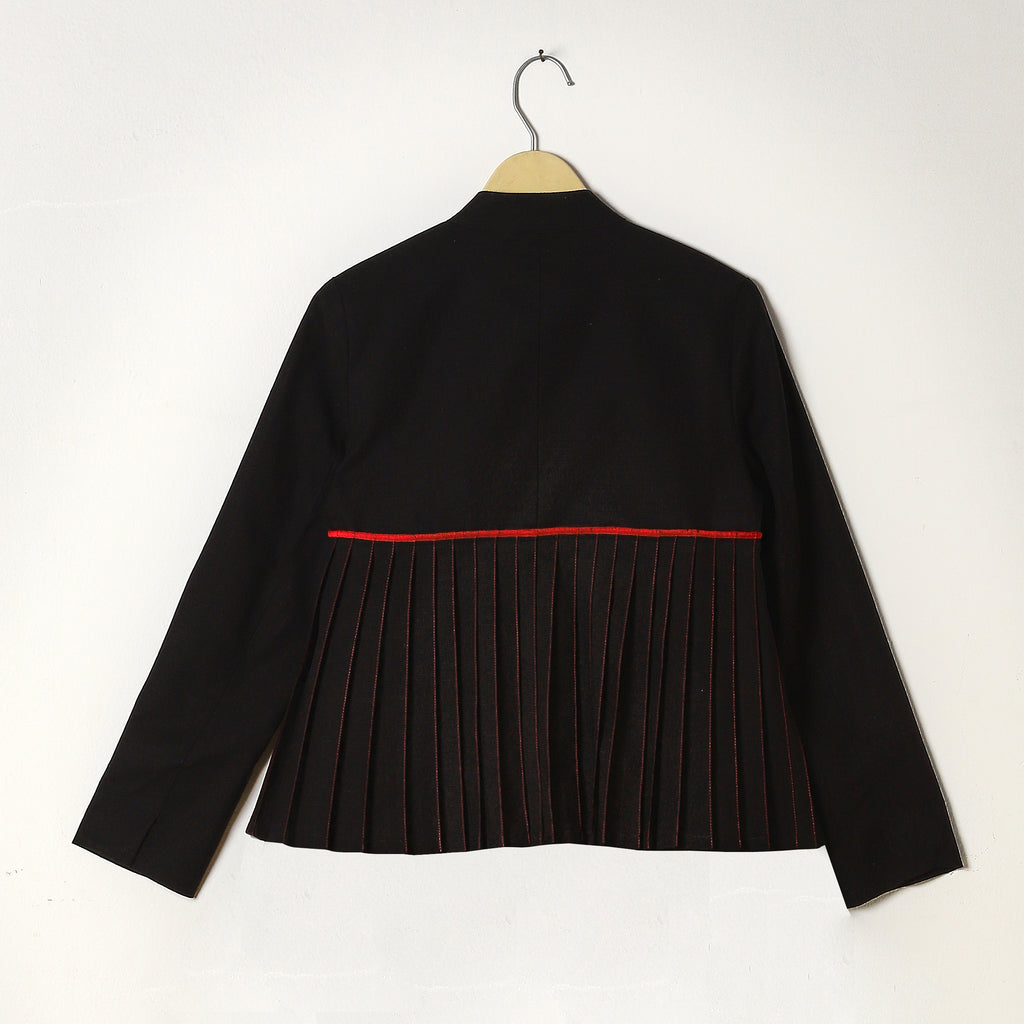 Black pleated dress with red trim on a hanger against a white background