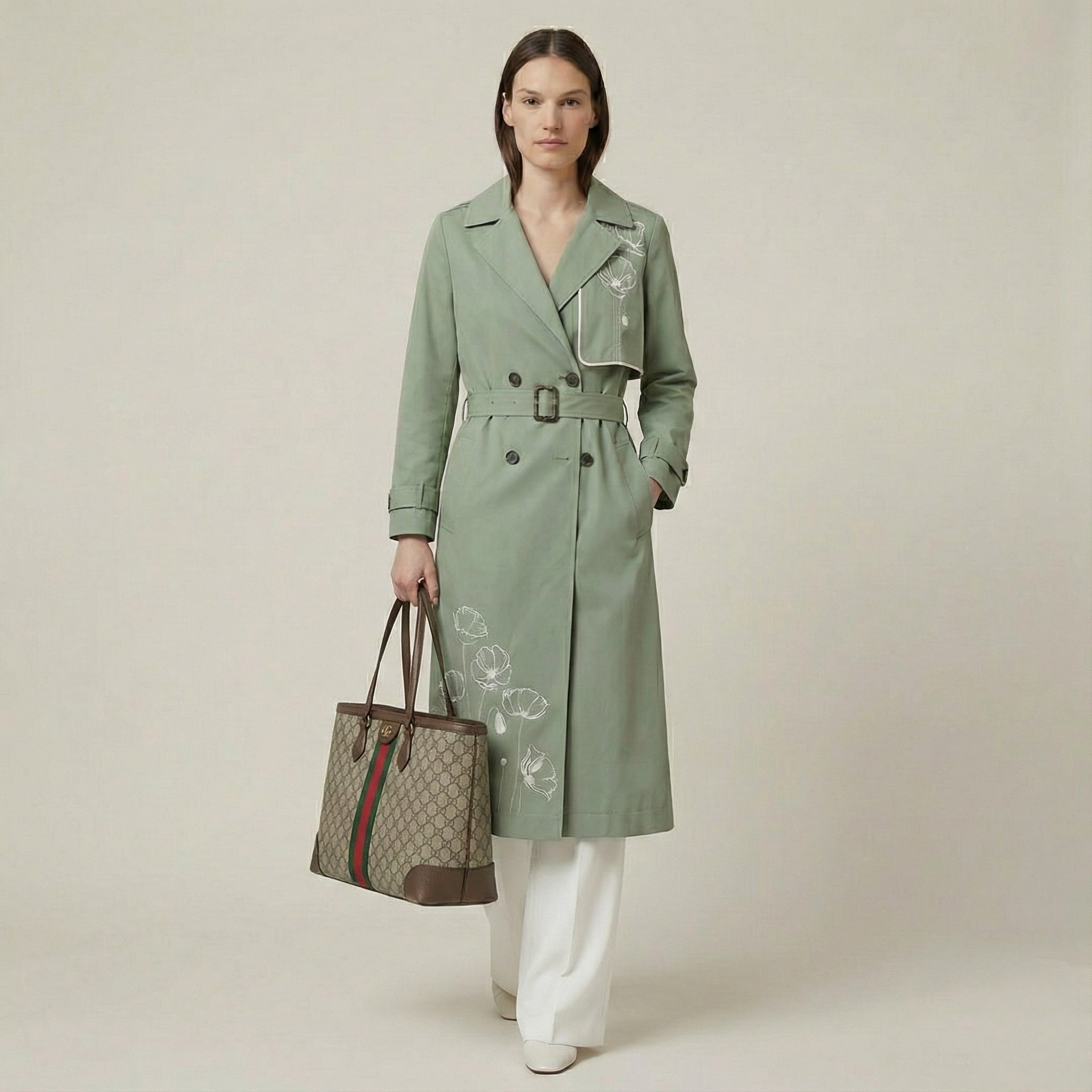 Woman wearing a green trench coat holding a Gucci handbag on a plain background