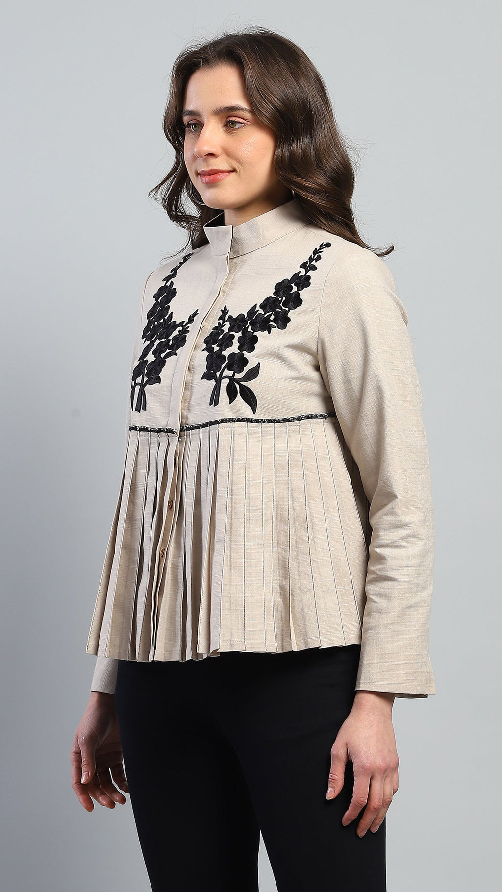 Woman wearing a beige blouse with black floral embroidery on a gray background
