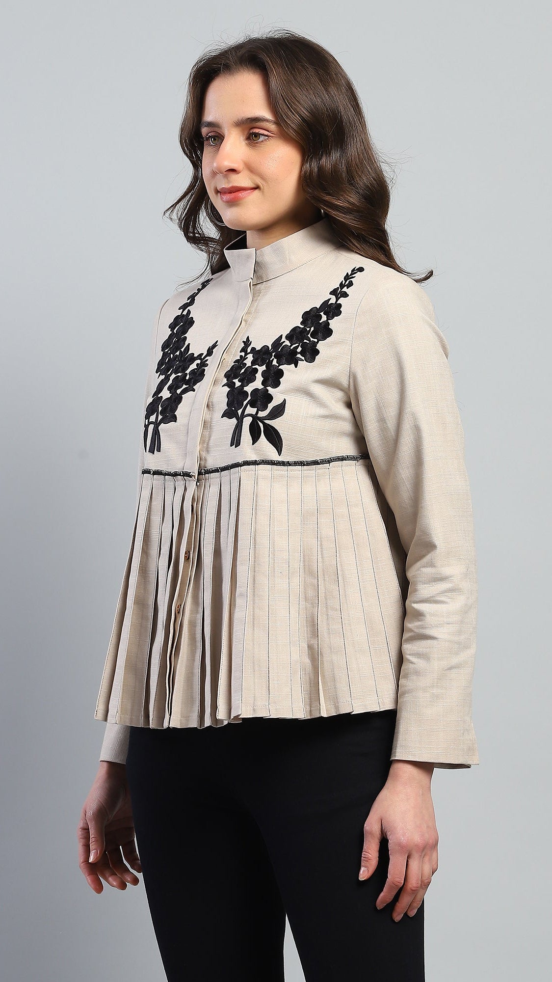 Woman wearing a beige blouse with black floral embroidery on a gray background