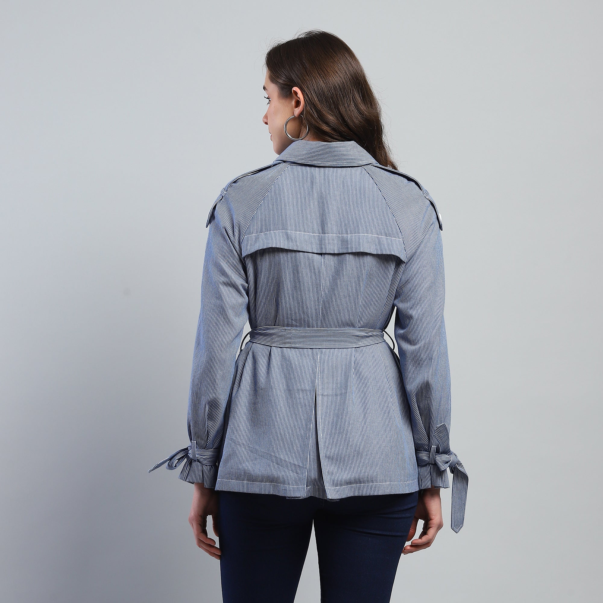 Woman wearing a gray jacket with a belt on a gray background