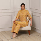 Woman in a yellow patterned outfit sitting on a white chair in a room with paneled walls.