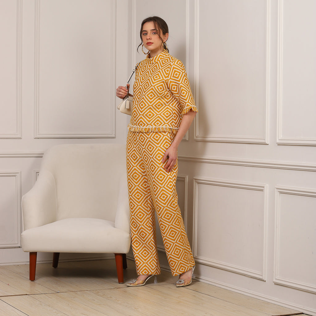 Woman in a yellow patterned outfit standing in a room with white paneled walls and a beige chair.