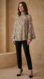 Woman wearing a leopard print blouse and black pants in a beige room.