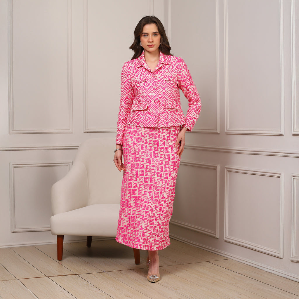 Woman wearing a pink patterned outfit standing in a room with a white armchair.