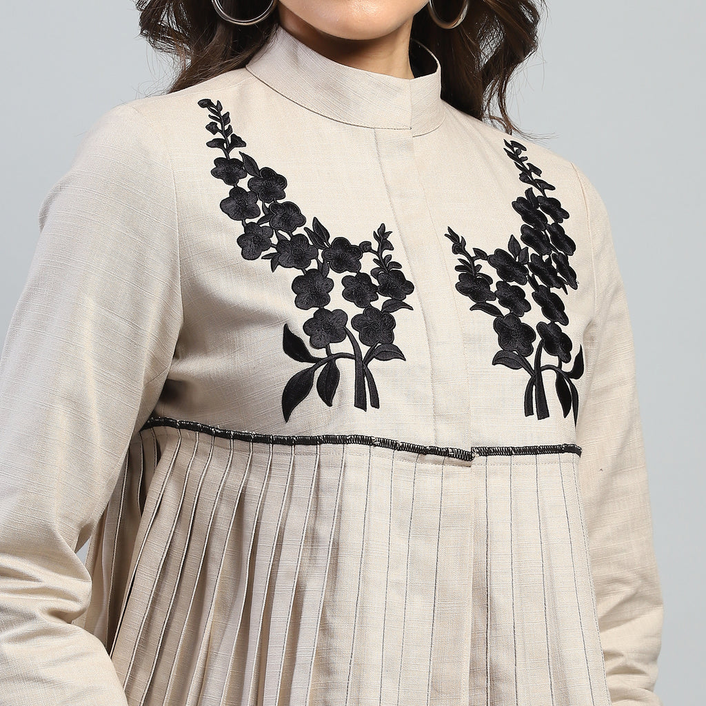 Beige outfit with black floral embroidery on a plain background