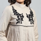 Beige outfit with black floral embroidery on a plain background