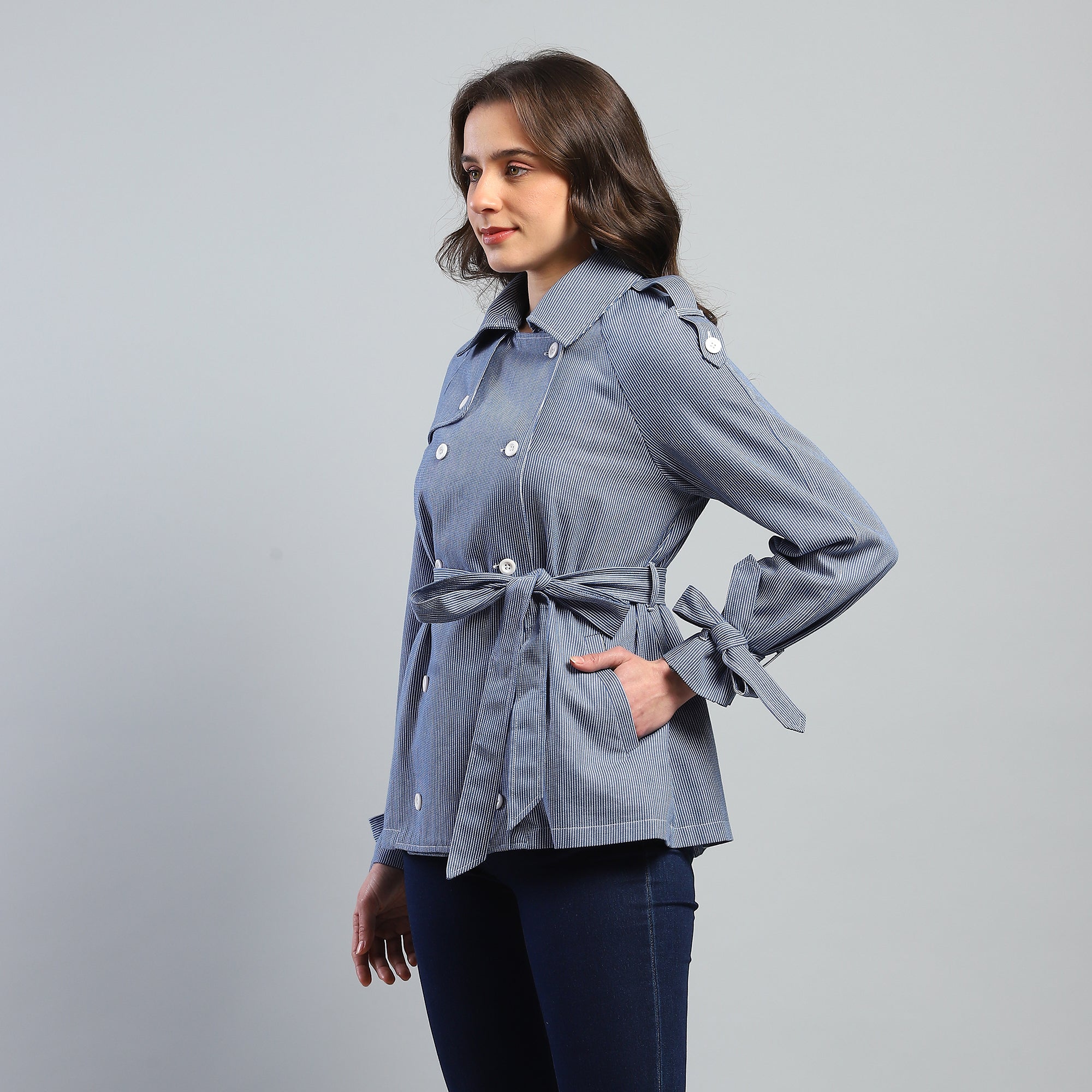Woman wearing a light blue denim jacket with a tie waist on a gray background