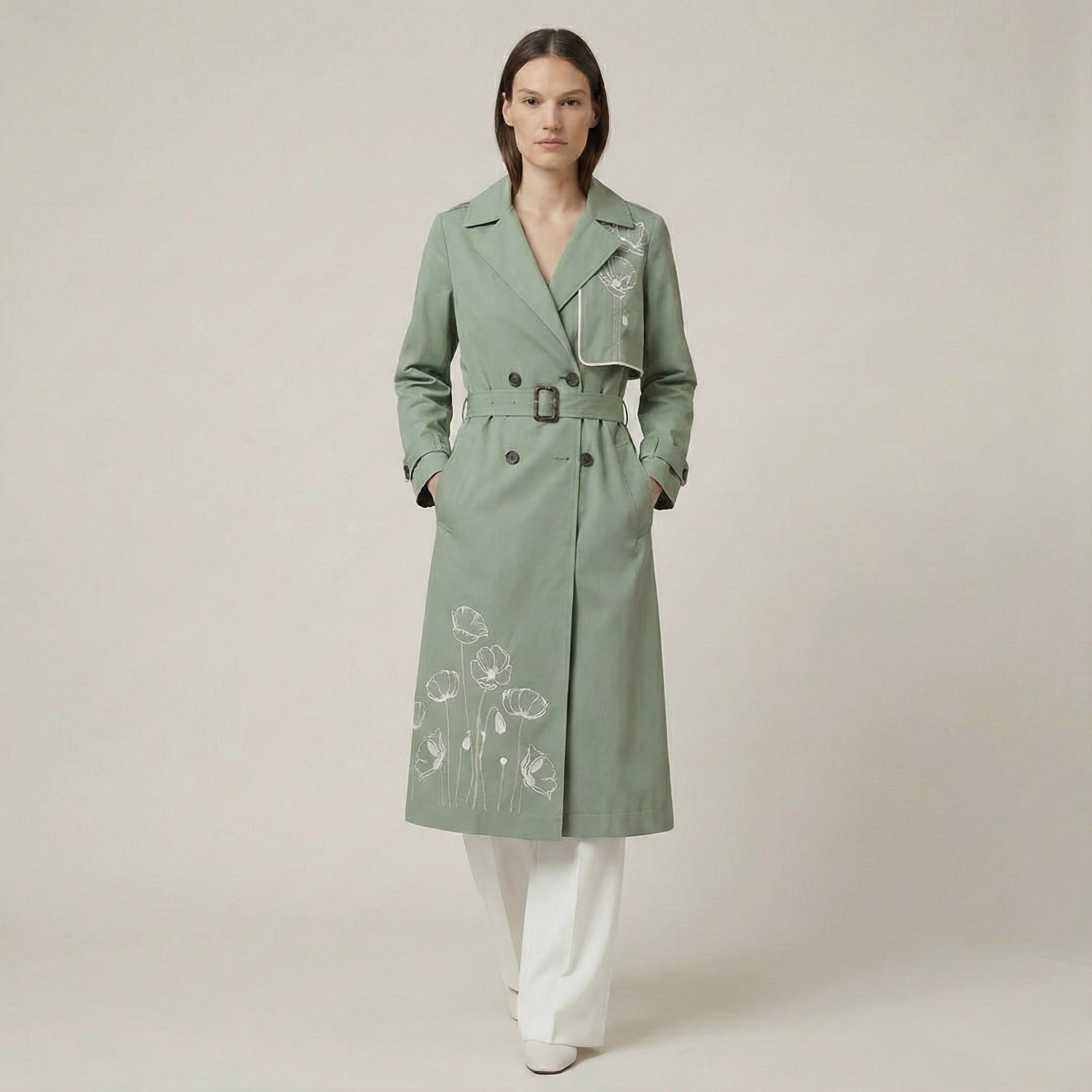 Woman wearing a green trench coat with floral embroidery on a beige background