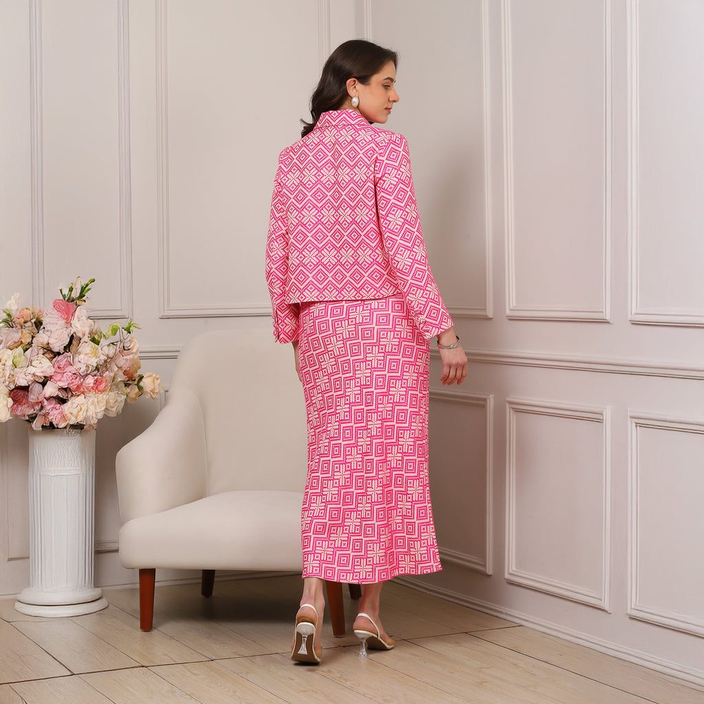 Woman in a pink patterned outfit standing in a room with a white armchair and floral arrangement.