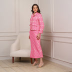 Woman wearing a pink patterned outfit standing in a room with a white armchair.