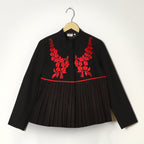 Black blouse with red floral embroidery on a hanger against a white background