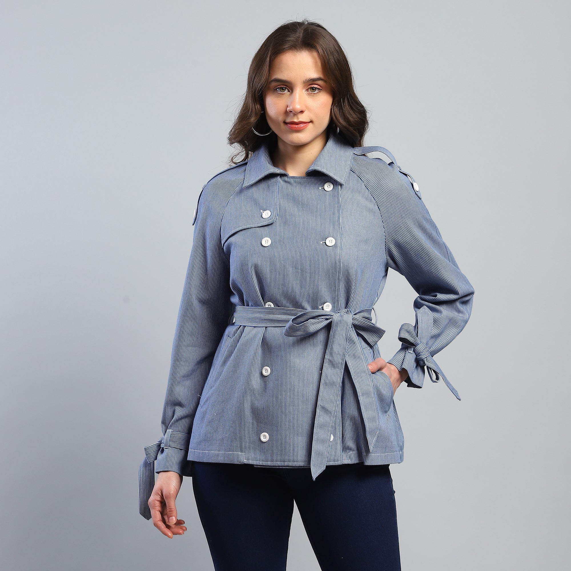 Woman wearing a blue denim jacket with a belt on a gray background