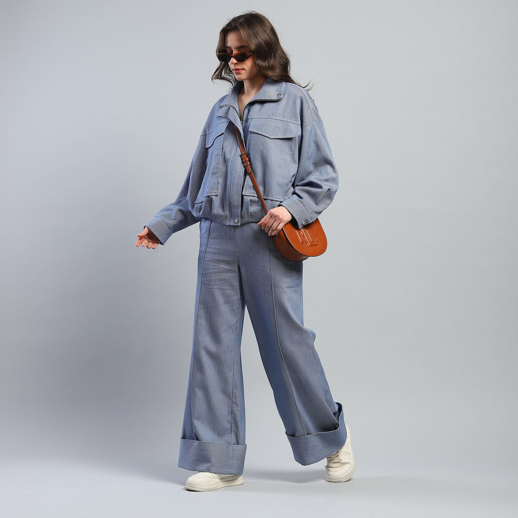 Person wearing a blue denim outfit with sunglasses and a brown bag on a gray background