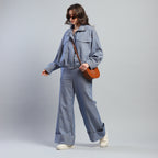 Person wearing a blue denim outfit with sunglasses and a brown bag on a gray background