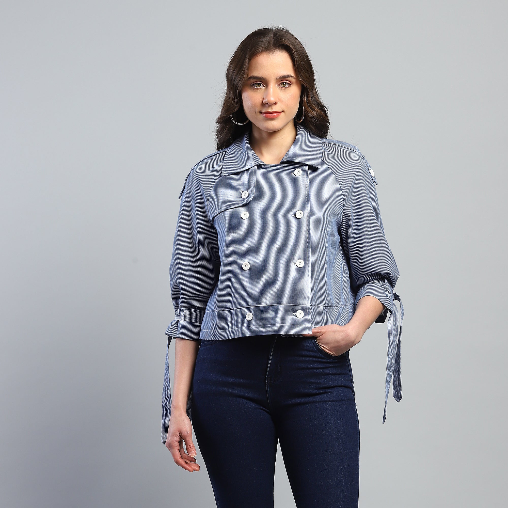 Woman wearing a blue denim jacket with white buttons on a gray background